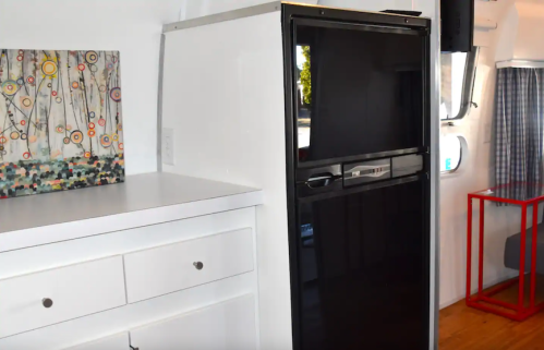 A modern kitchen interior featuring a black refrigerator next to a white cabinet and colorful wall art.