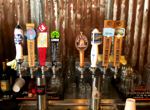 A row of colorful beer taps featuring various craft beers in a rustic bar setting.