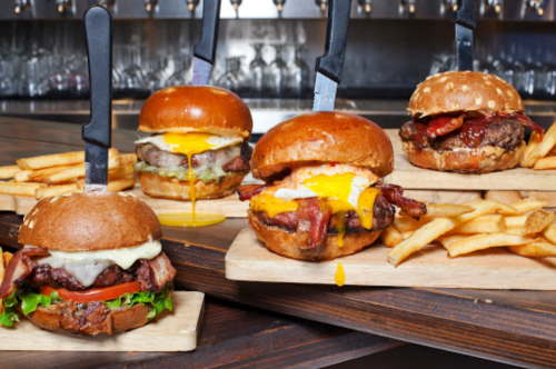 A variety of gourmet burgers with toppings and fries, served on wooden boards with knives inserted in the buns.