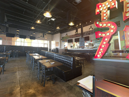 Interior of a modern restaurant featuring black booths, wooden tables, and a vibrant sign with lights.