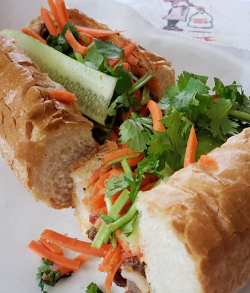 A close-up of a sandwich filled with carrots, cucumber, and cilantro in a crusty baguette.