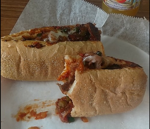 A close-up of a partially eaten sandwich filled with meat, vegetables, and sauce, resting on white paper.