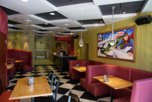 A colorful restaurant interior with red booths, checkered floor, and a large artwork on the wall.