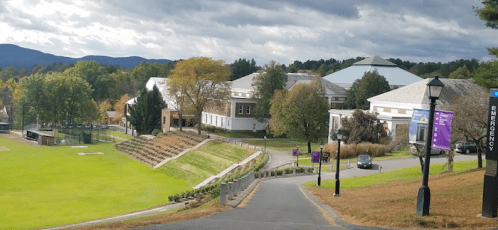 A scenic view of a campus with buildings, a sports field, and trees under a cloudy sky.