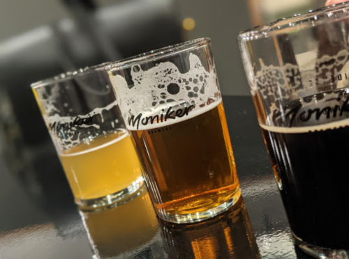 Three glasses of beer in varying shades, with frothy tops, sitting on a reflective surface.