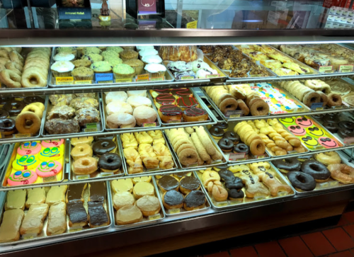 A display case filled with a variety of colorful donuts and pastries, showcasing different shapes and toppings.