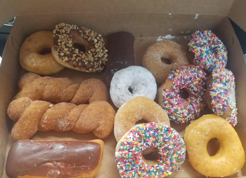 A box of assorted donuts, including glazed, chocolate, sprinkled, and powdered varieties, arranged neatly.