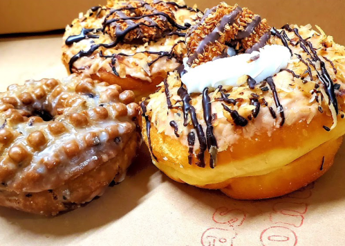 Three delicious donuts: one with chocolate drizzle, one topped with coconut and caramel, and a glazed donut with a waffle texture.