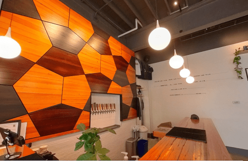 Interior of a modern café featuring a geometric wooden wall, pendant lights, and a wooden counter with plants.