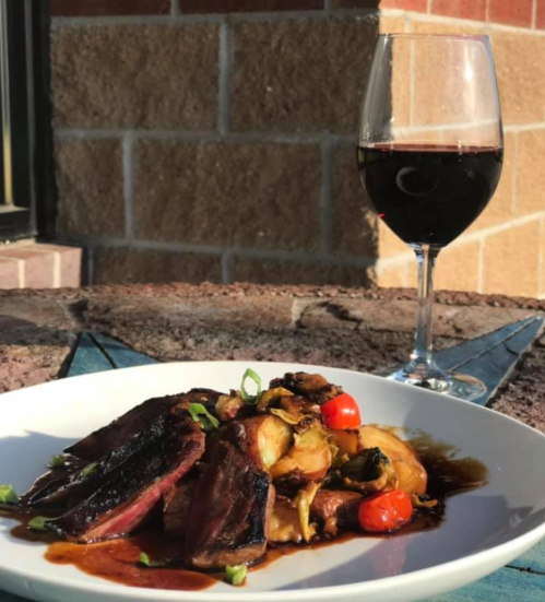 A plate of grilled meat with roasted vegetables and cherry tomatoes, accompanied by a glass of red wine.