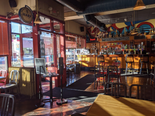 A brightly lit restaurant interior with colorful decor, bar area, and empty tables and chairs.