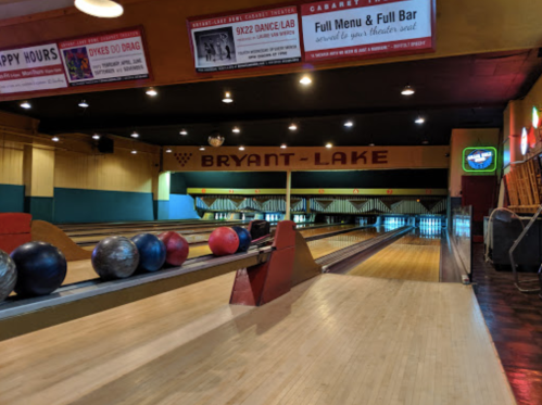 A bowling alley with colorful balls lined up on the lane, featuring a sign that reads "BRYANT-LAKE" in the background.