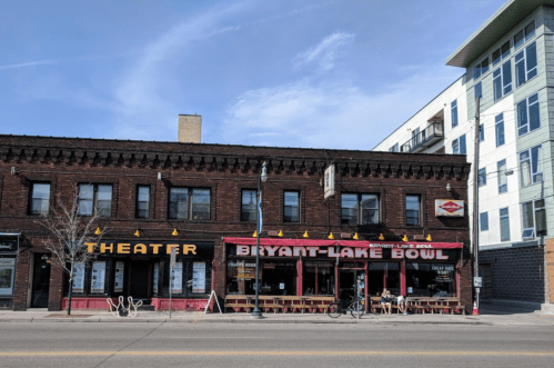A brick building featuring a theater and Bryant-Lake Bowl, with outdoor seating and a clear blue sky above.