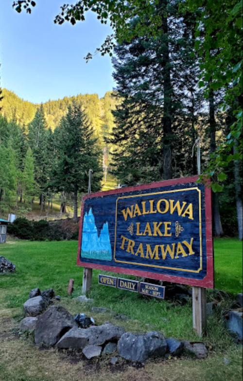 Sign for Wallowa Lake Tramway surrounded by trees and mountains, indicating it's open daily.