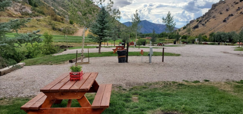 A scenic outdoor area with picnic tables, trees, and mountains in the background under a cloudy sky.