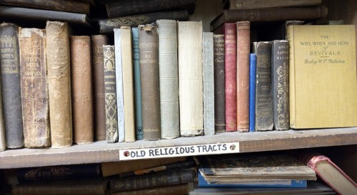 A shelf filled with old books, including religious tracts and titles on revivals, showcasing worn spines and varied colors.