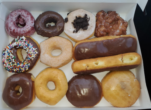 A box of assorted donuts, including glazed, chocolate-covered, and sprinkled varieties, arranged neatly.