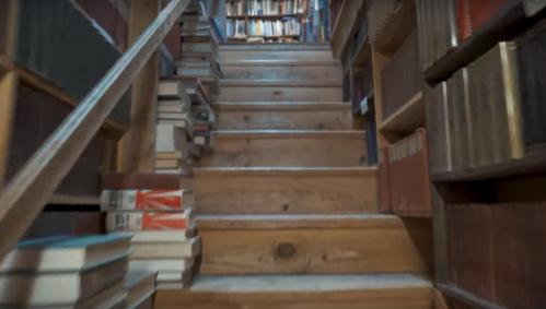 A wooden staircase lined with books on either side, leading up to a cozy library filled with shelves of books.
