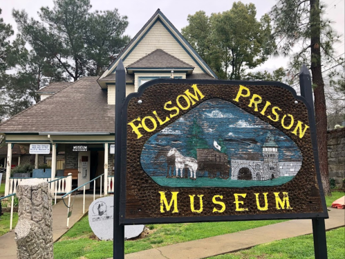 Sign for Folsom Prison Museum in front of a historic building surrounded by trees.