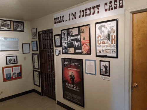 A wall display featuring Johnny Cash memorabilia, including photos, articles, and a poster, next to a prison cell door.