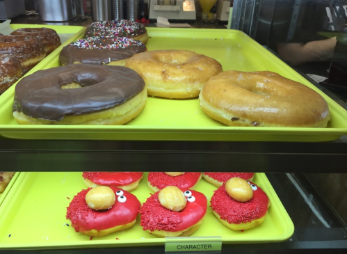 A display of donuts: two glazed, one chocolate-covered, and two red Elmo-themed donuts with sprinkles and candy eyes.