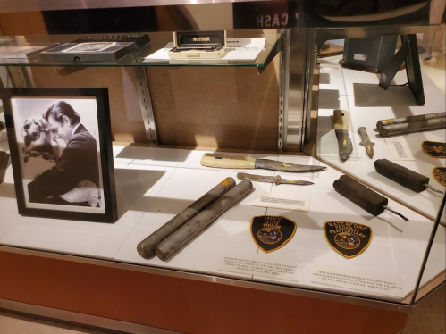 Display case featuring historical weapons, police badges, and a framed black-and-white photo of a couple.
