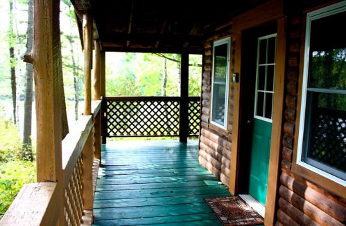 A wooden porch with a green door, surrounded by trees and natural light filtering through.