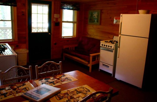 Cozy wooden kitchen with a dining table, a couch, a fridge, and a stove, featuring warm lighting and rustic decor.