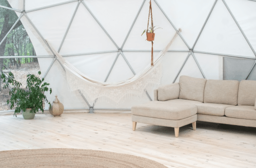 Cozy interior of a geodesic dome featuring a hammock, a sofa, a plant, and natural wood flooring.