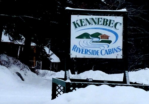 Sign for Kennebec Riverside Cabins, surrounded by snow, featuring a river and cabin illustration.