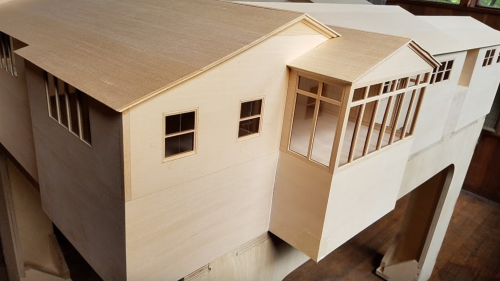 A detailed architectural model of a building with multiple sections and large windows, made from light wood.