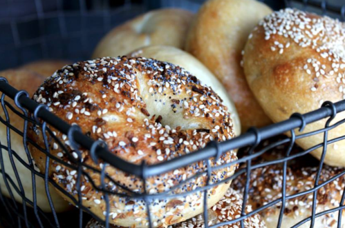 A wire basket filled with freshly baked bagels topped with sesame seeds.