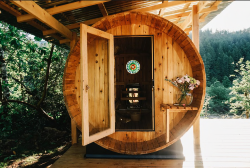 A wooden round cabin with an open door, featuring a stained glass window and a vase of flowers inside.