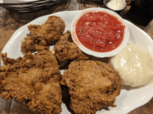 A plate of crispy fried chicken with a side of mashed potatoes and a bowl of tomato salsa.