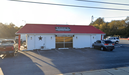 A white restaurant building with a red roof and a star on the side, parked cars in front, and trees in the background.