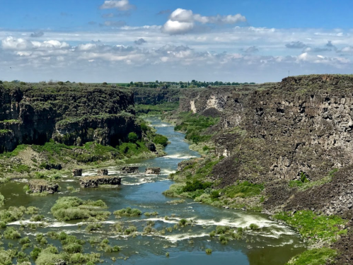 A scenic view of a river winding through rocky cliffs and lush greenery under a partly cloudy sky.