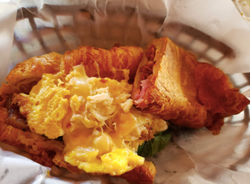 A flaky croissant sandwich filled with scrambled eggs, cheese, and shredded chicken, served in a basket.