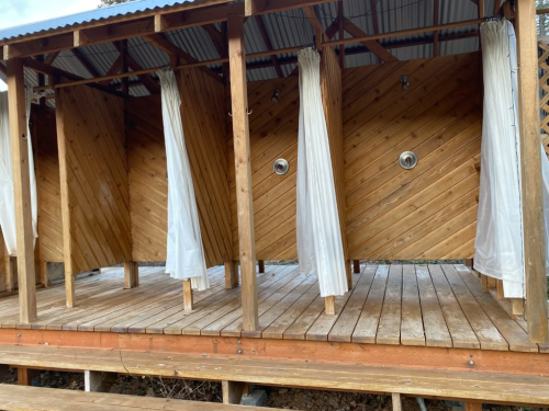 Wooden outdoor shower stalls with white curtains, set on a wooden deck under a roof.