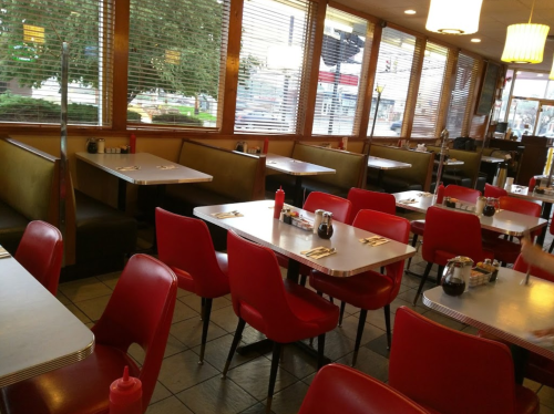 A cozy diner interior with red chairs, tables set for dining, and large windows letting in natural light.