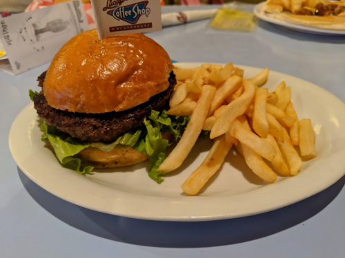 A juicy burger with lettuce on a bun, served with a side of golden French fries on a white plate.