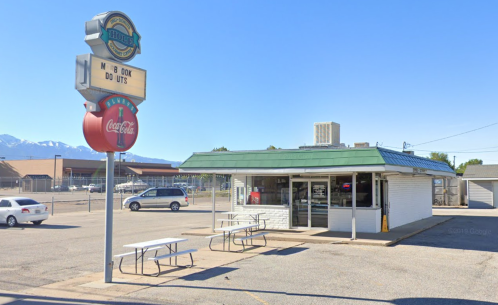 A small diner with a green roof and outdoor seating, featuring a vintage sign and nearby parking lot.