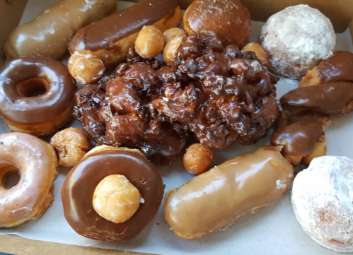 A variety of donuts, including glazed, chocolate-covered, and a large chocolate cluster, arranged in a box.