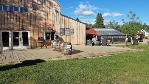 A wooden building with a deck, barrels, and a sign reading "ORDER," surrounded by green grass and blue skies.