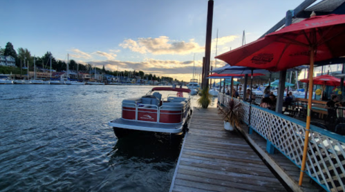 A boat docked by a waterfront restaurant, with a scenic view of the water and clouds at sunset.