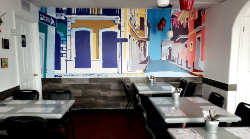 Colorful mural of a street scene on a restaurant wall, with tables and chairs arranged for dining.