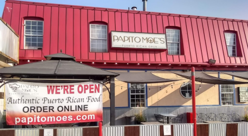 Exterior of Papito Moe's, a Puerto Rican restaurant, featuring a red roof and a sign stating "We're Open" with a banner.
