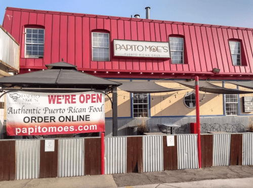 Exterior of Papito Moe's, a Puerto Rican restaurant, featuring a red roof and a sign stating "We're Open" with online ordering info.