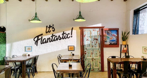 Bright restaurant interior with wooden tables, green lamps, and a mural saying "It's Flantastic!" on the wall.
