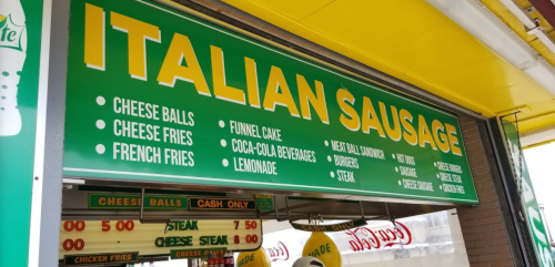 Sign for an eatery featuring "Italian Sausage" and menu items like cheese balls, funnel cake, and beverages.