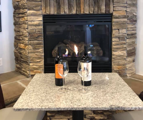 A cozy table with two wine bottles and glasses in front of a stone fireplace.